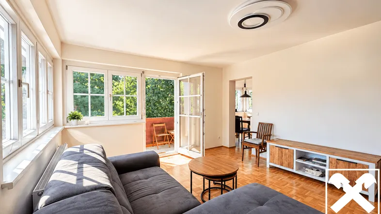 Helles Wohnzimmer mit Parkettboden, Balkonzugang und Blick ins Grüne durch große Fenster.