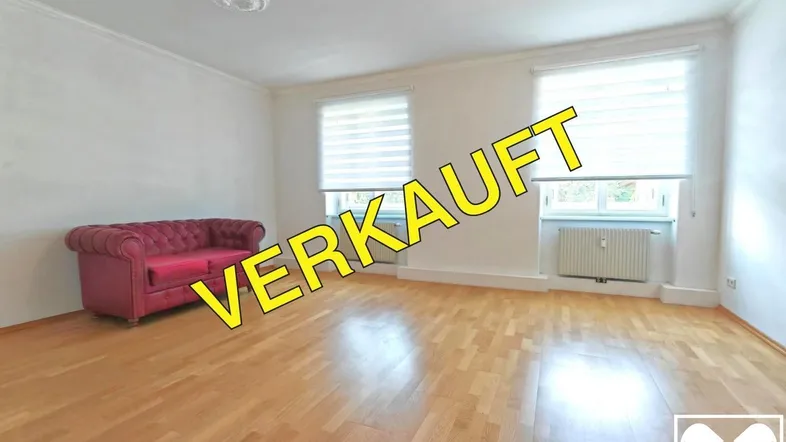 Helles Wohnzimmer mit Parkettboden, weiß gestrichenen Wänden und einem roten Sofa.