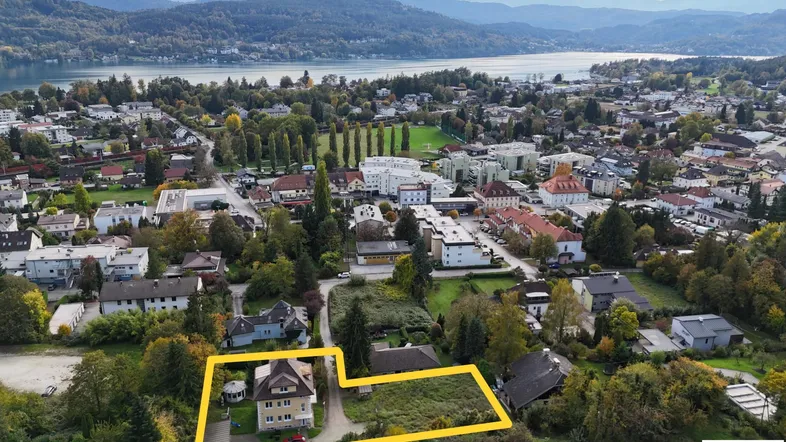Luftaufnahme des Grundstücks mit Haus, umgeben von Bäumen und Blick auf den See und die Berge.