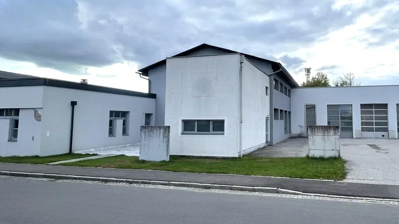 Außenansicht eines modernen Geschäftsgebäudes mit mehreren Garagentoren und einem gepflegten Vorplatz unter bewölktem Himmel.