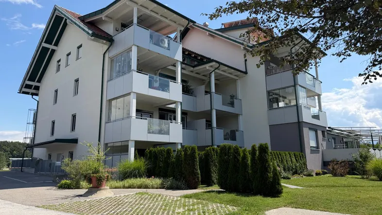 Mehrstöckiges Wohngebäude mit mehreren Balkonen und gepflegter Grünanlage unter blauem Himmel.