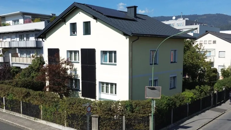 Freistehendes Einfamilienhaus mit Photovoltaikanlage und grüner Hecke an der Straßenecke.