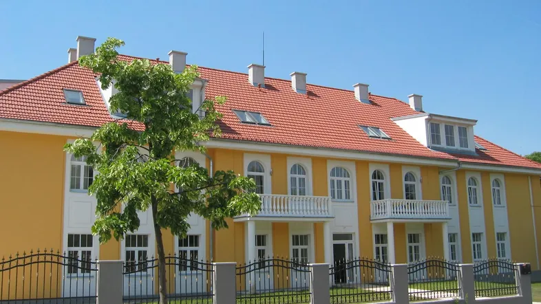 Gelbe Fassade eines Mehrfamilienhauses mit rotem Ziegeldach und weißen Balkonen.