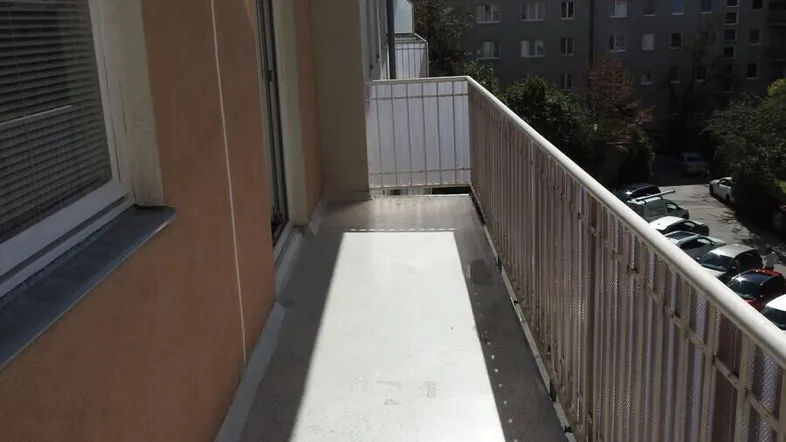 Langer Balkon mit Blick auf die umliegenden Gebäude und den Parkplatz.