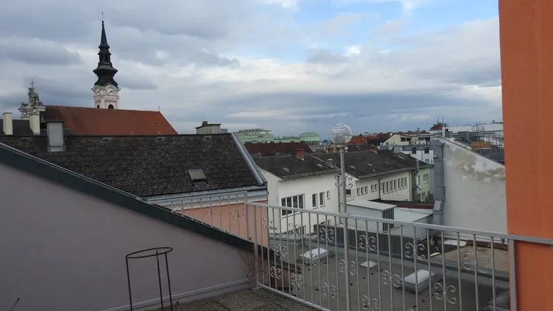 Dachterrasse mit Blick über die Dächer der Stadt und Kirchtürme unter bewölktem Himmel.