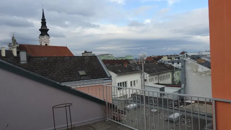 Blick von der Terrasse über die Dächer der Stadt mit Kirchturm im Hintergrund und bewölktem Himmel.