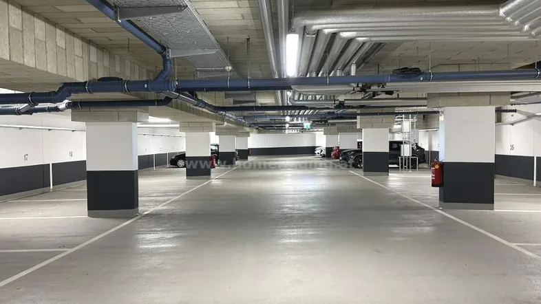 Geräumige Tiefgarage mit vielen markierten Stellplätzen, Betonwänden und sichtbaren Installationen an der Decke.