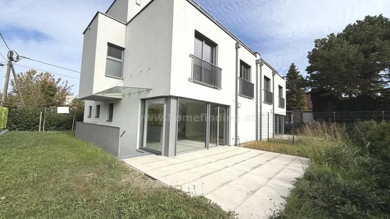 Moderne weiße Doppelhaushälfte mit großer Terrasse und Gartenbereich unter blauem Himmel.