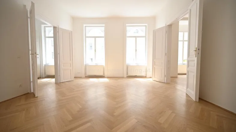 Heller Raum mit Fischgrätparkett und hohen Fenstern, der mehrere Zimmer miteinander verbindet.