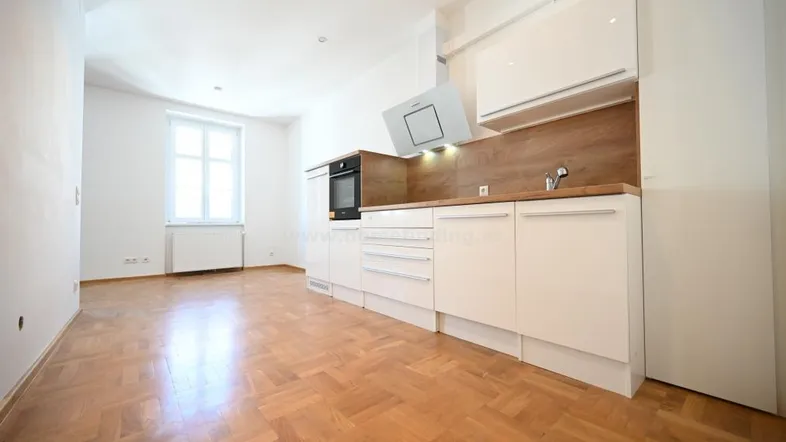 Moderne, helle Küchenzeile mit weißen Schränken und Holzakzenten in einem leeren Raum mit Parkettboden.