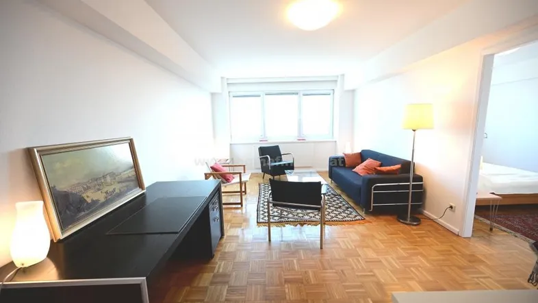 Geräumiges Wohnzimmer mit Parkettboden, großen Fenstern und einem Schreibtischbereich.