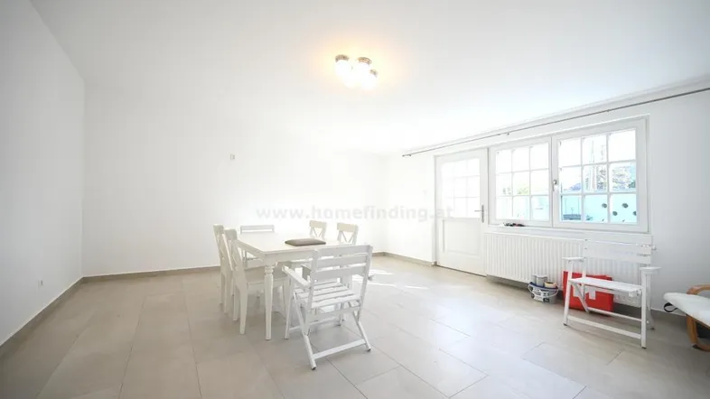 Heller, geräumiger Wohn-Essbereich mit Fliesenboden, großem Fenster und Zugang zum Außenbereich.