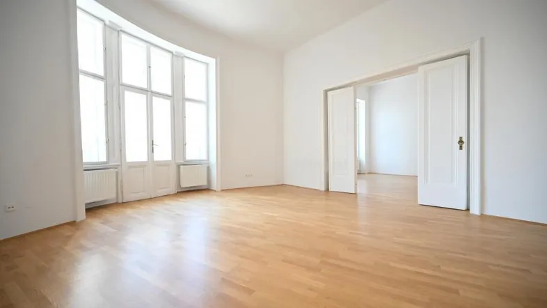 Helles Wohnzimmer mit großen Fenstern, Parkettboden und hohen Decken, bereit zur individuellen Gestaltung.