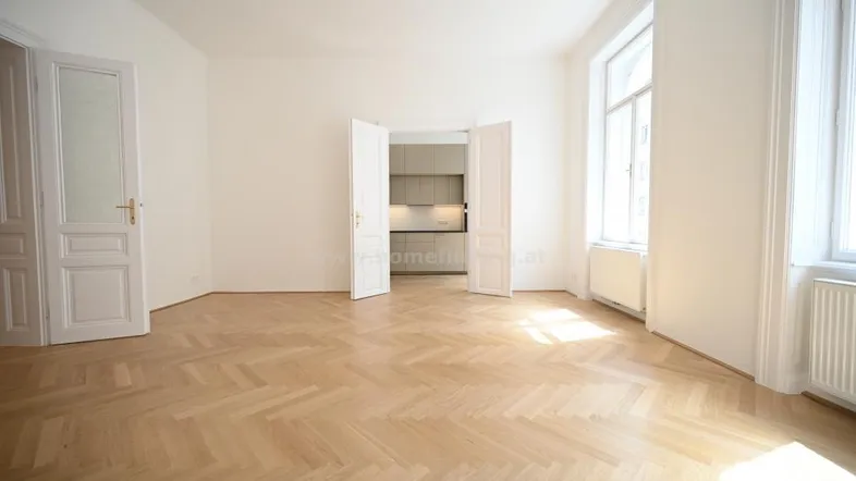 Geräumiges Wohnzimmer mit elegantem Fischgrätparkett und viel Tageslicht durch hohe Fenster.