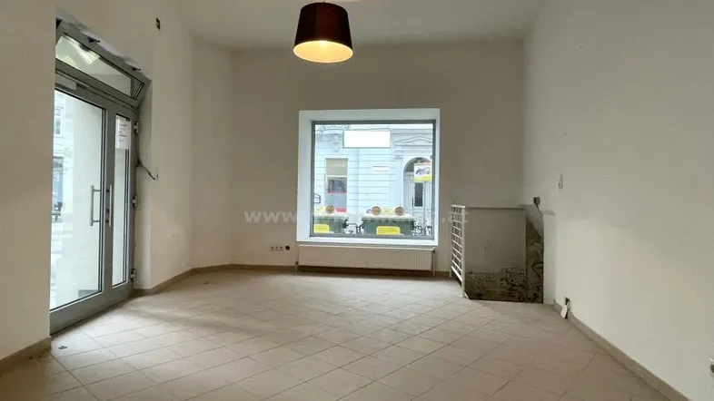 Heller, leerer Raum mit Fliesenboden und großen Fenstern zur Straße, bereit zur Gestaltung.