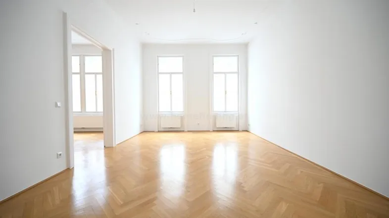 Helles, leeres Zimmer mit Fischgrätparkett und hohen Fenstern, bereit zur individuellen Gestaltung.