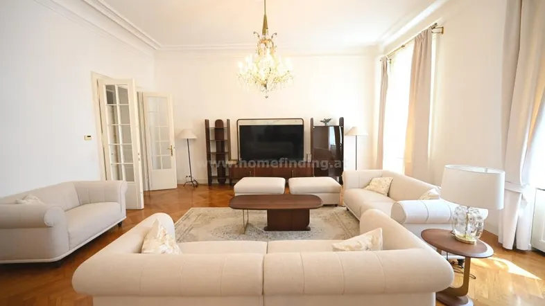 Helles Wohnzimmer mit eleganten Sofas, Parkettboden und einem opulenten Kronleuchter, der den Raum erhellt.