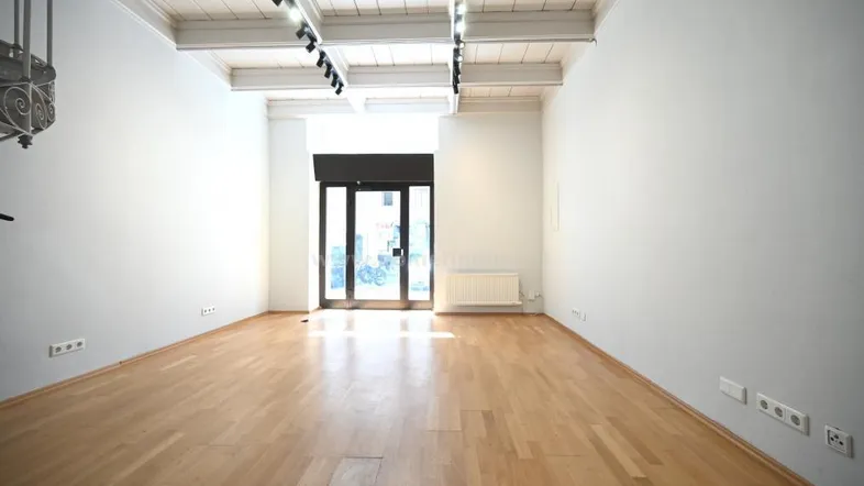 Helles Zimmer mit Holzboden, sichtbaren Deckenbalken und einer großen Glastür zum Eingangsbereich.