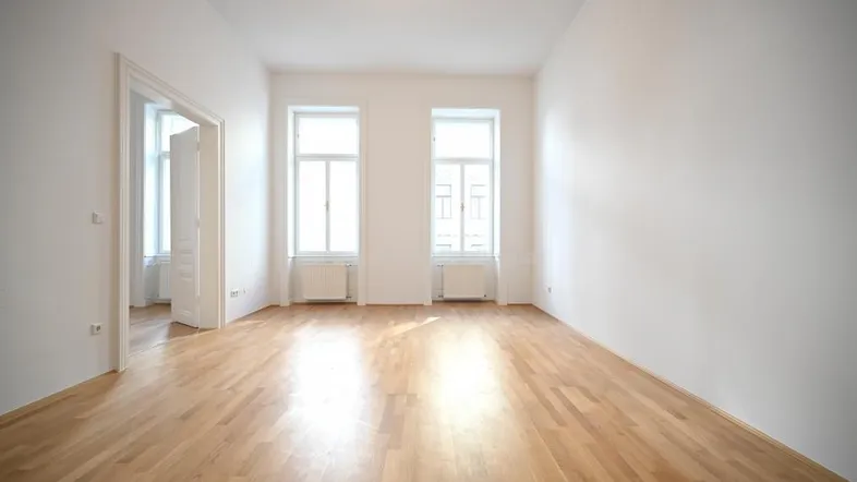 Helles Zimmer mit Parkettboden und zwei großen Fenstern, bereit zur individuellen Gestaltung.