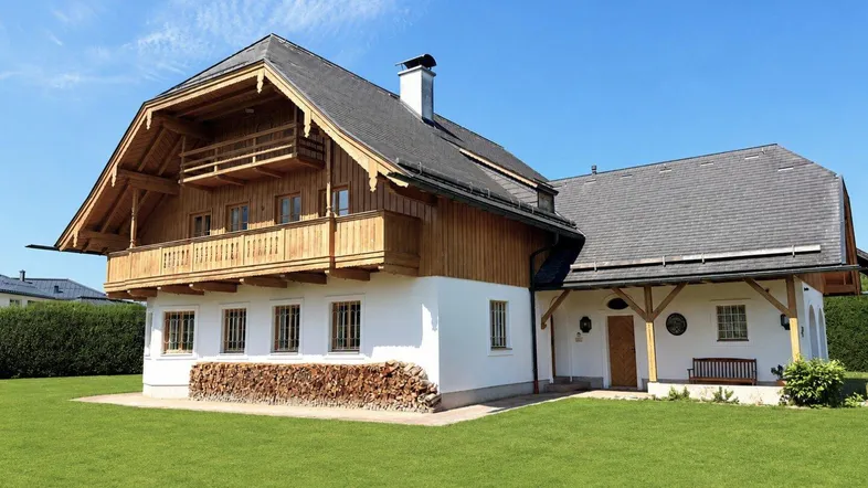 Traditionelles Landhaus mit Holzbalkonen und weißer Fassade, umgeben von einem gepflegten Rasen.