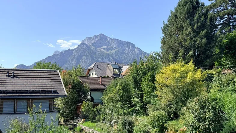 Panoramablick auf die umliegende Berglandschaft mit grünen Bäumen und Häusern unter blauem Himmel.