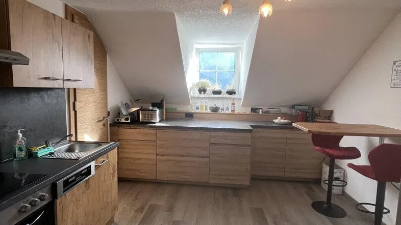 Gemütliche Küche im Dachgeschoss mit Holzelementen, Frühstücksbar und Dachfenster für natürliches Licht.