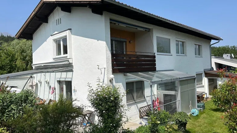 Weißes Wohnhaus mit Balkon, Wintergarten und gepflegtem Gartenbereich unter blauem Himmel.
