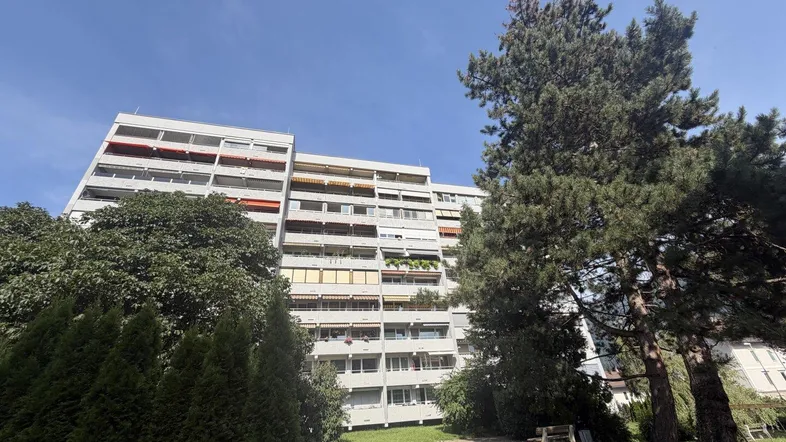 Mehrstöckiges Wohngebäude mit Balkonen und umliegender Grünfläche unter blauem Himmel.