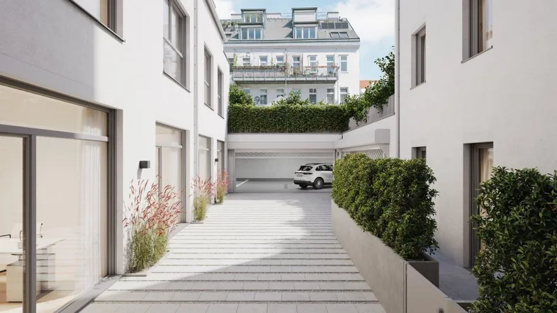 Zufahrt zu einer Tiefgarage zwischen modernen weißen Gebäuden mit gepflegter Bepflanzung und klarem Himmel.