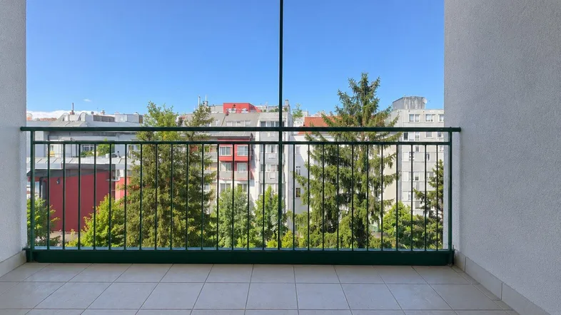 Heller Balkon mit Fliesenboden und Blick auf Bäume und umliegende Gebäude.