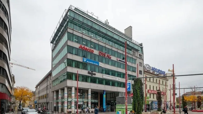 Modernes Bürogebäude mit Glasfassade und Werbeschildern an einer belebten Straße in urbaner Umgebung.