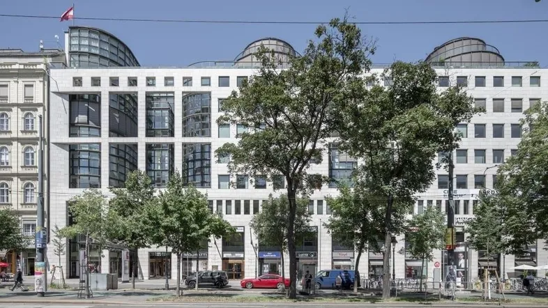 Modernes Bürogebäude mit großen Glasflächen und Geschäften im Erdgeschoss an einer belebten Straße.