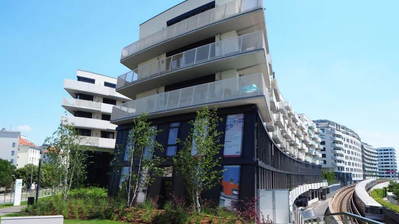 Modernes Wohngebäude mit geschwungener Fassade, Balkonen und Blick auf Bahngleise.