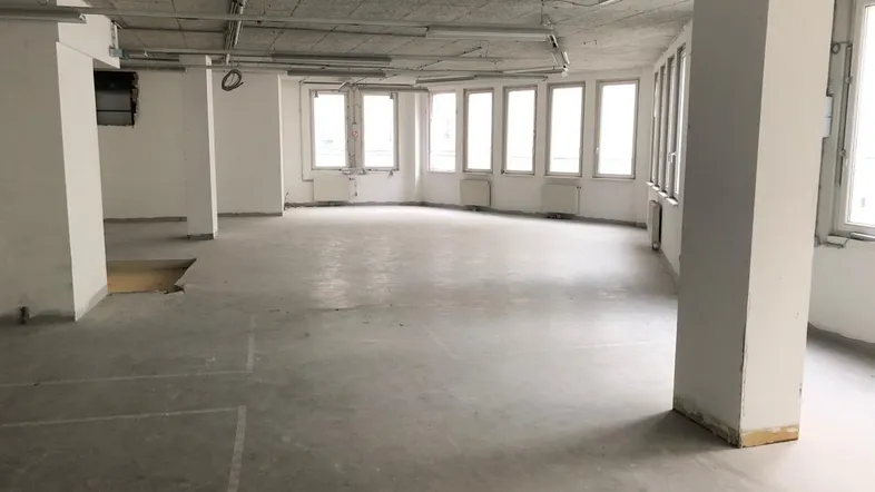 Großer, leerer Büroraum mit vielen Fenstern und Betonboden, bereit für den Ausbau.
