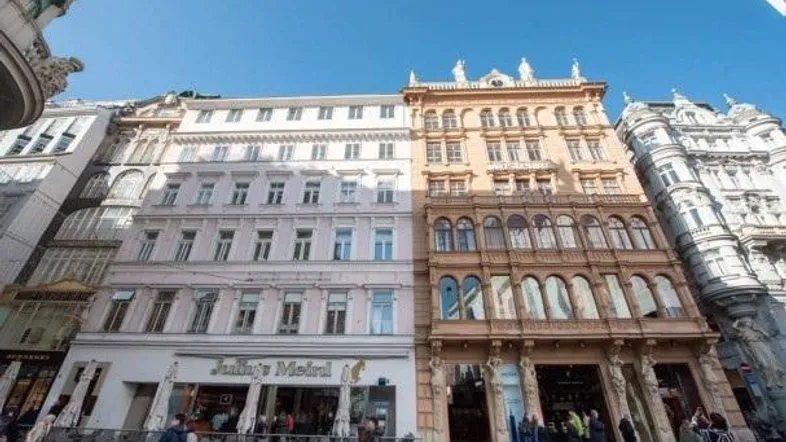Historische Gebäudefronten in Wien mit Geschäften im Erdgeschoss und klarem Himmel.