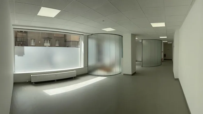 Geräumiger, heller Büroraum mit großen Fenstern, modernen Deckenleuchten und eleganten Glasabtrennungen.