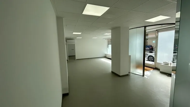 Geräumiger, heller Büroraum mit abgehängter Decke, Einbauleuchten und großen Fenstern zur Straße.