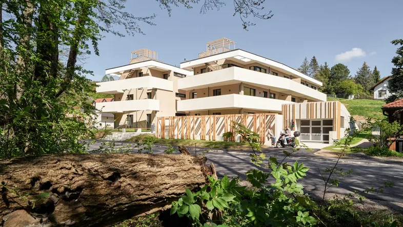 Modernes Mehrfamilienhaus mit hellen Fassaden und Balkonen, eingebettet in eine grüne Umgebung.