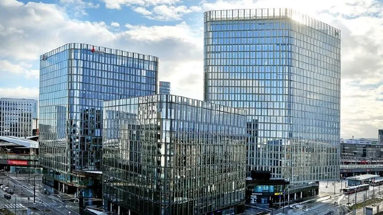 Moderne Bürogebäude mit Glasfassaden und urbaner Umgebung unter einem bewölkten Himmel.