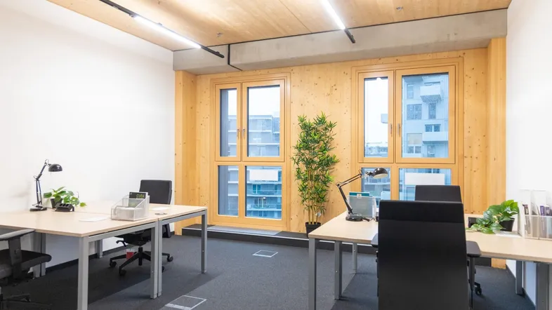Modernes Büro mit mehreren Arbeitsplätzen, Holzwänden und Teppichboden, bietet Blick auf umliegende Gebäude.