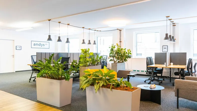 Moderner Großraumbüro-Arbeitsbereich mit ergonomischen Stühlen, Schreibtischen und vielen Pflanzen für eine angenehme Arbeitsatmosphäre.