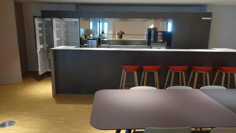 Moderne Teeküche mit dunklen Schränken, integriertem Kühlschrank und Holzboden, ideal für Pausen.