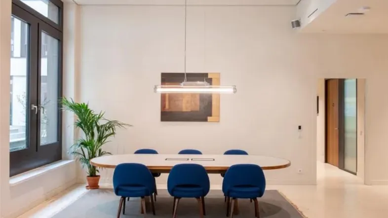Moderner Konferenzraum mit ovalem Tisch, blauen Stühlen und großen Fenstern, ideal für Besprechungen.