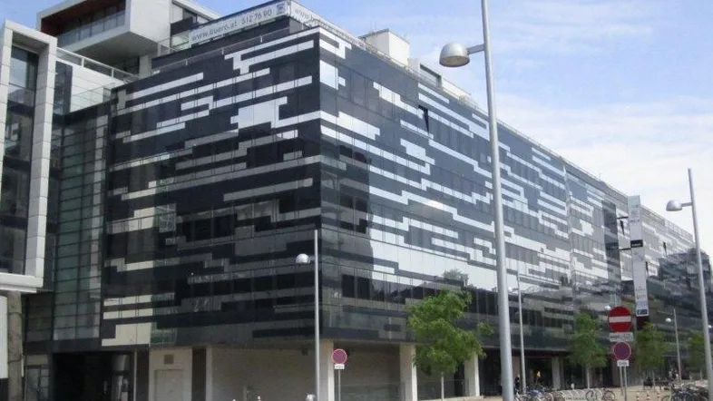 Modernes Bürogebäude mit markanter Glasfassade und horizontalen Streifenmustern an einer städtischen Straße.