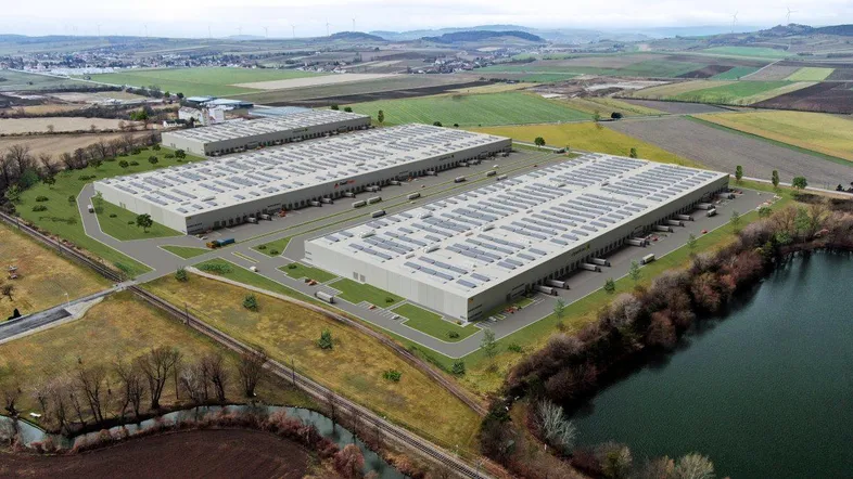 Luftaufnahme eines modernen Logistikparks mit mehreren großen Lagerhallen neben einem See und Feldern.