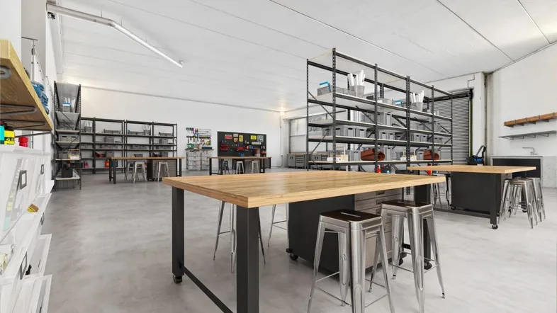 Geräumiger, heller Werkstattraum mit großen Arbeitstischen, Regalen und Betonboden, ideal für kreative Projekte.