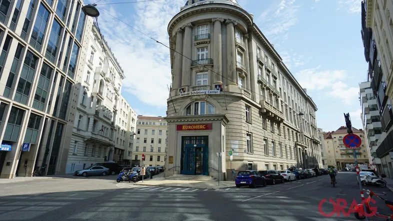 Historisches Gebäude an einer Straßenecke mit klassischer Architektur und vielen Fenstern, umgeben von städtischem Leben.