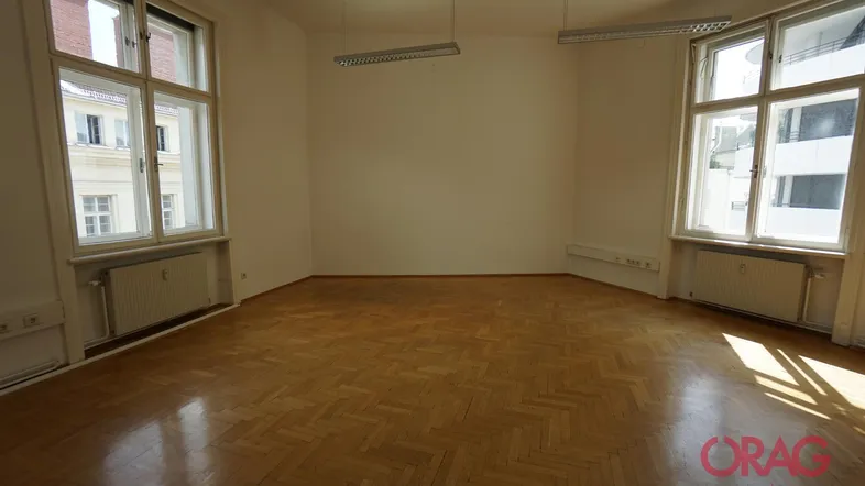 Heller, leerer Raum mit Fischgrätparkett und großen Fenstern, ideal für Büronutzung.