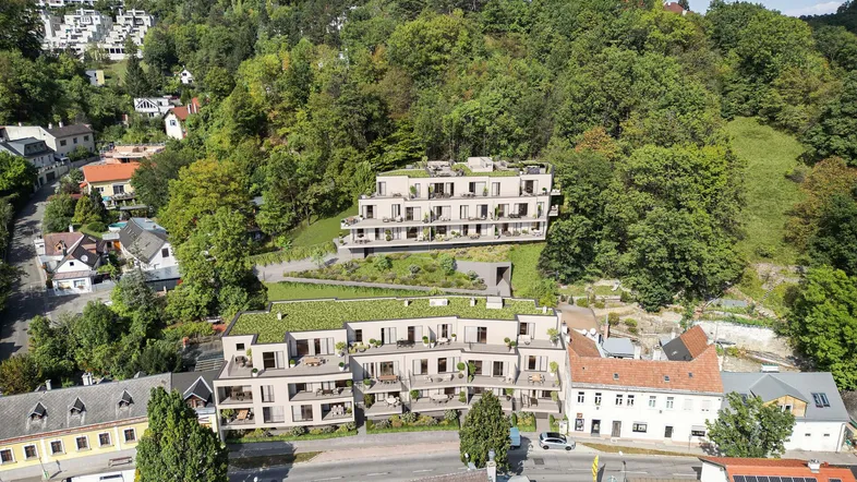 Moderne Wohnanlage in Hanglage, umgeben von viel Grün und anderen Häusern, mit Balkonen und Terrassen.
