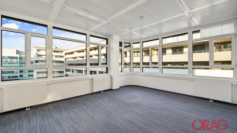 Geräumiges Büro mit großen Fenstern, die viel Tageslicht hereinlassen und einen Blick auf umliegende Gebäude bieten.